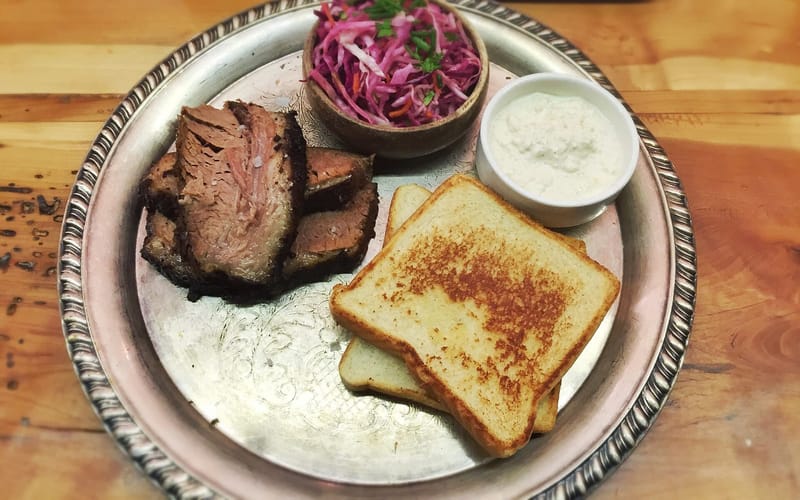 Sliced smoked brisket with white bread, horseradish, and slaw