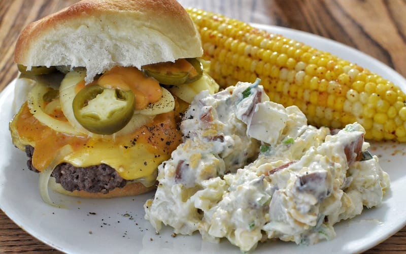 A cheeseburger served with potato salad and sweet corn