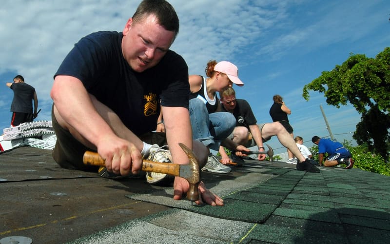 A worker nailing shingles onto the roof of a house